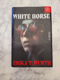 The book cover of 'White Horse' by Erika T. Wurth, featuring a dark cover with a horse's face and red and white text, placed on a white marble surface.