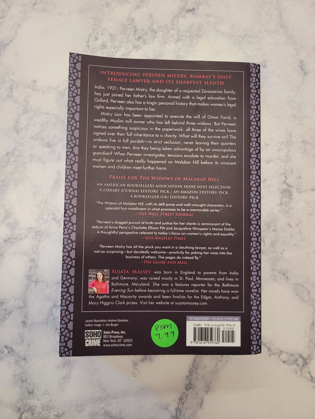 The back cover of a book , displayed flat on a white and gray marble surface. The cover is dark brown with white text, a decorative border, a barcode, and a green price sticker.
