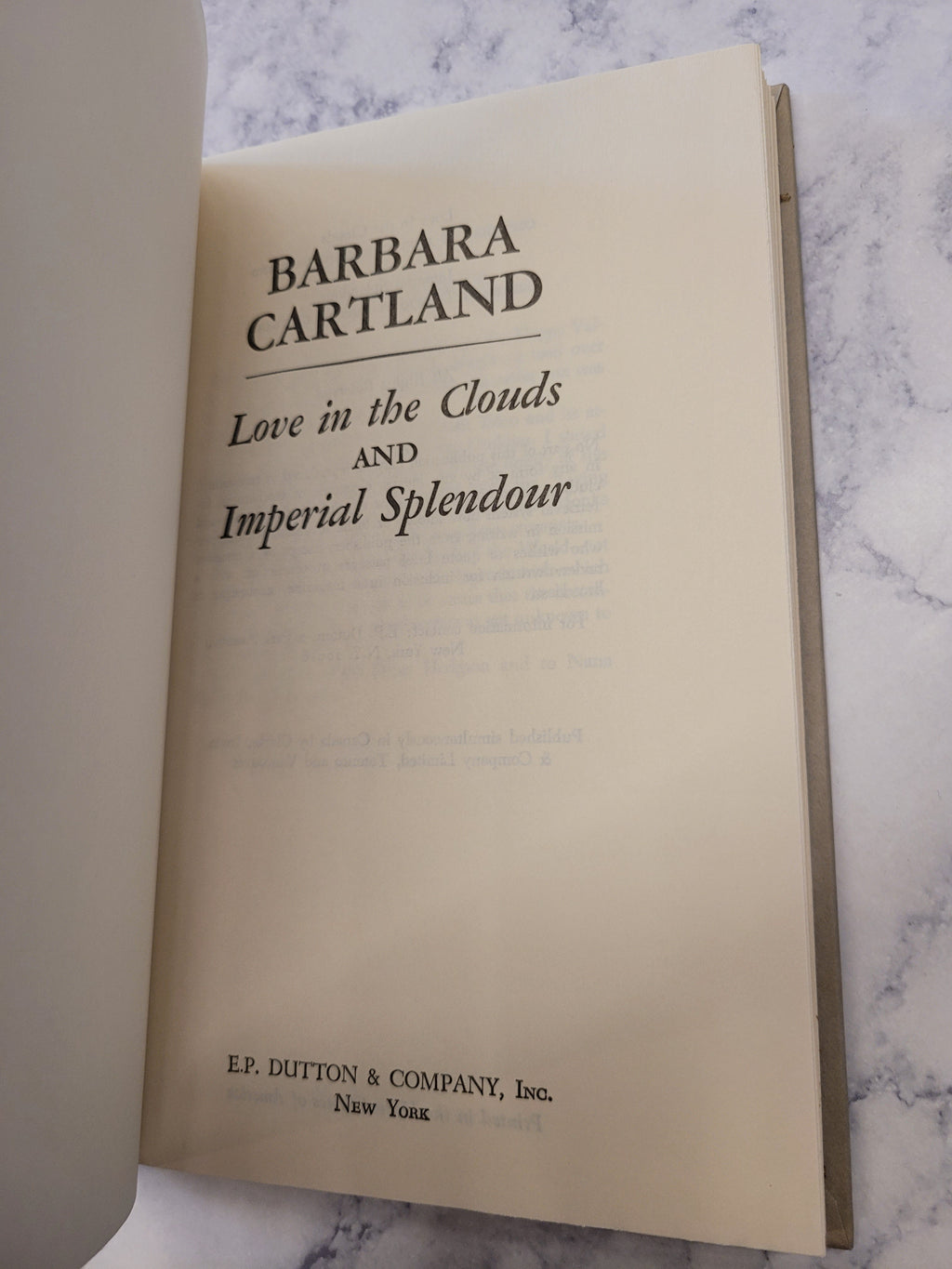A close-up of a book's title page for 'Love in the Clouds and Imperial Splendour' by Barbara Cartland, published by EP Edition & Company, Inc., placed on a white marble surface.