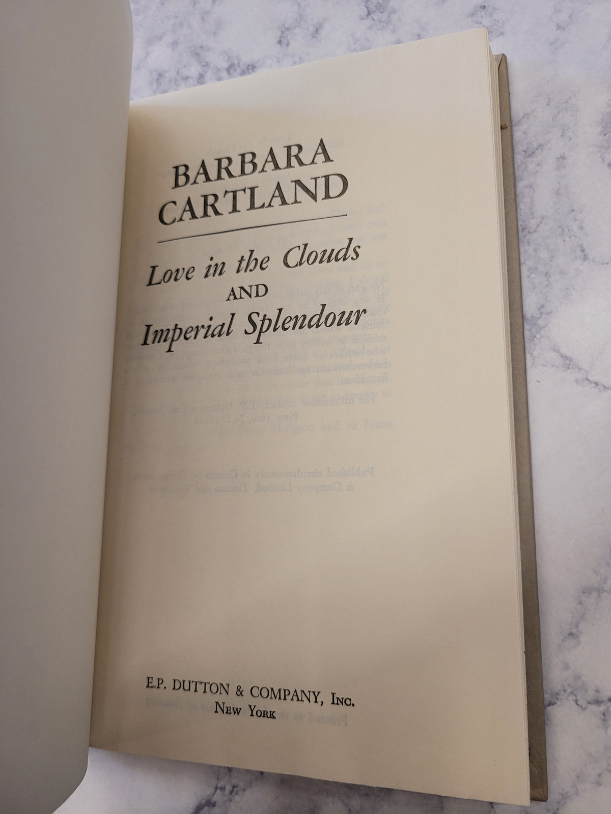 A close-up of a book's title page for 'Love in the Clouds and Imperial Splendour' by Barbara Cartland, published by EP Edition & Company, Inc., placed on a white marble surface.