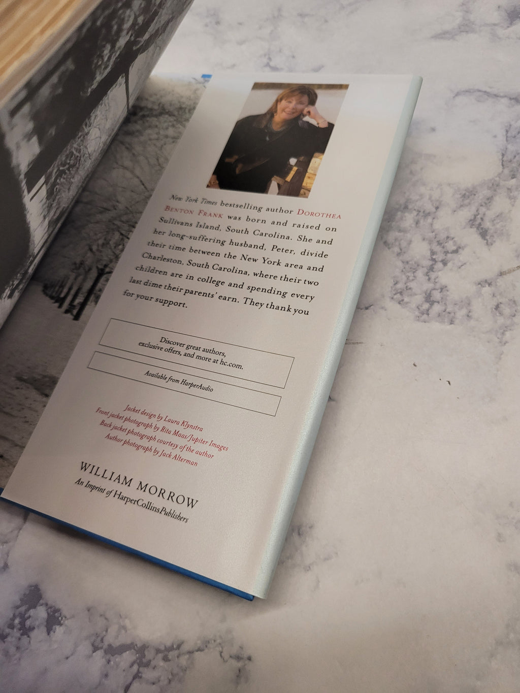 An open book or booklet lying on a light marble-like surface, showing the interior back page with a small portrait photo, blocks of text.