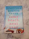 The book cover of 'Same Beach, Next Year' by Dorothea Benton Frank, placed on a light gray and white marble surface. The cover features a light blue sky background with red text and illustrations of people on a beach.