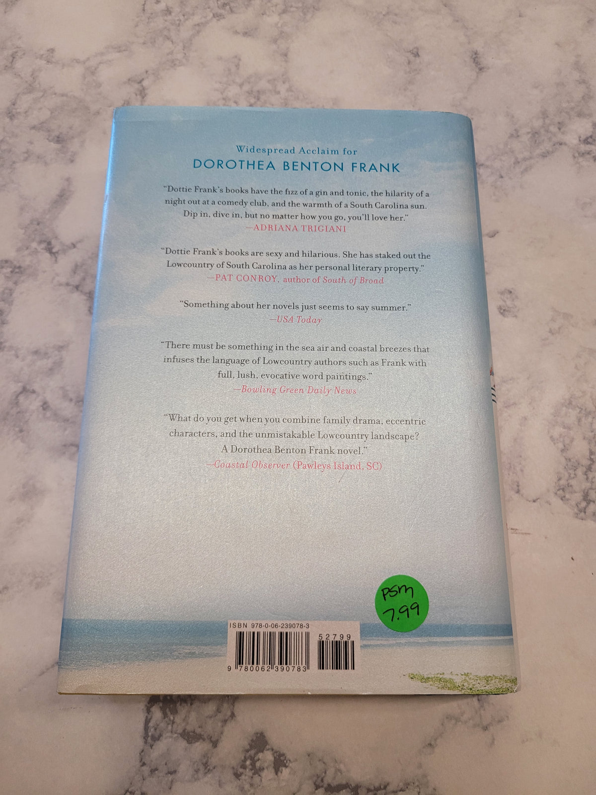 The back cover of a book featuring a light blue and white design with a green 'petite' sticker, photographed on a white marble surface.