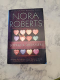 The book cover of 'Lovers & Dreamers' by Nora Roberts, featuring a dark purple background with pastel-colored heart illustrations, placed on a white marble surface.