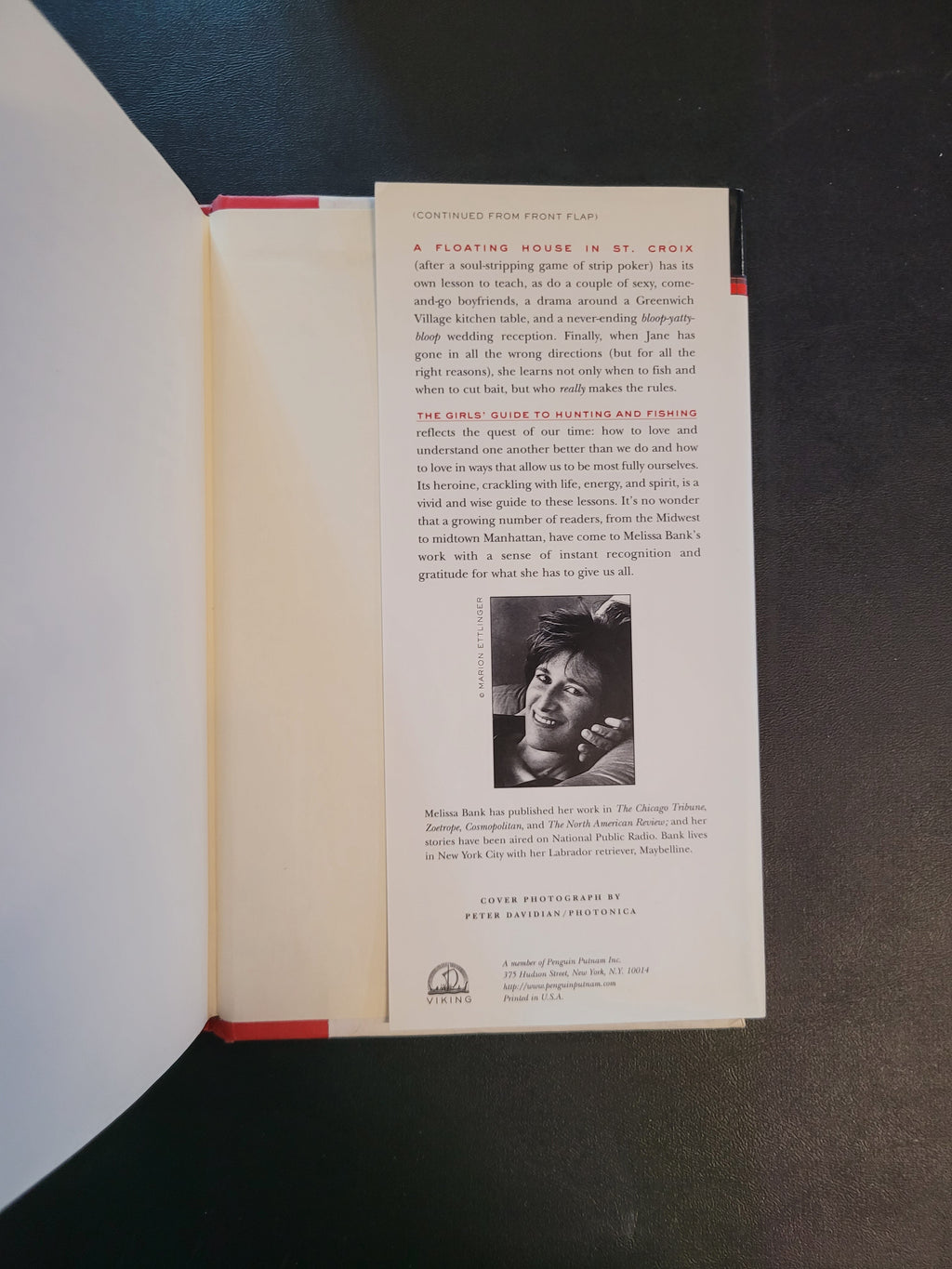 An open book showing a printed interior page with text, a small black-and-white portrait photograph, and red binding edges, photographed against a dark background.