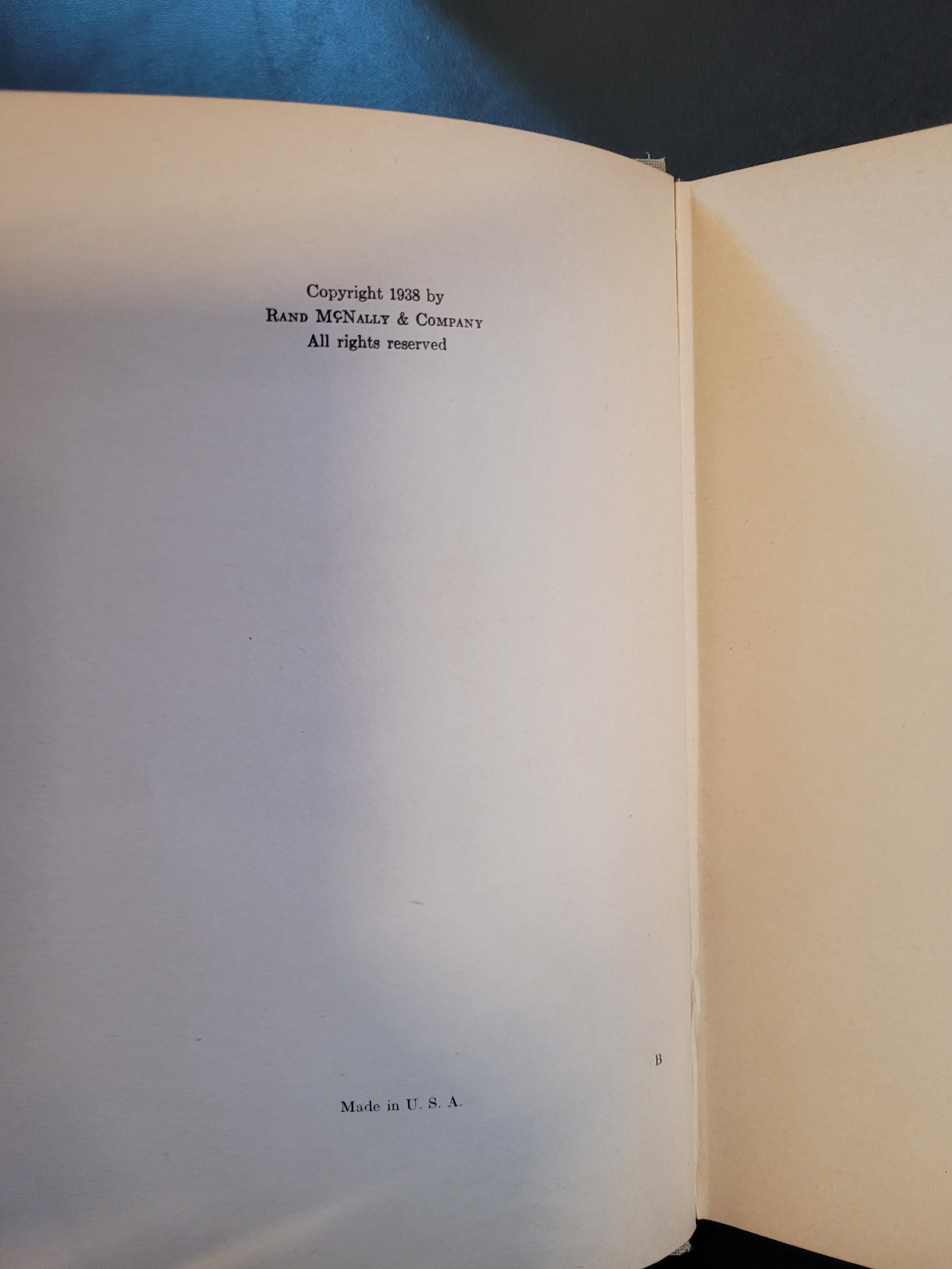 An open book showing blank cream-colored pages with small black printed text on the right and left margins, photographed against a dark blue background.