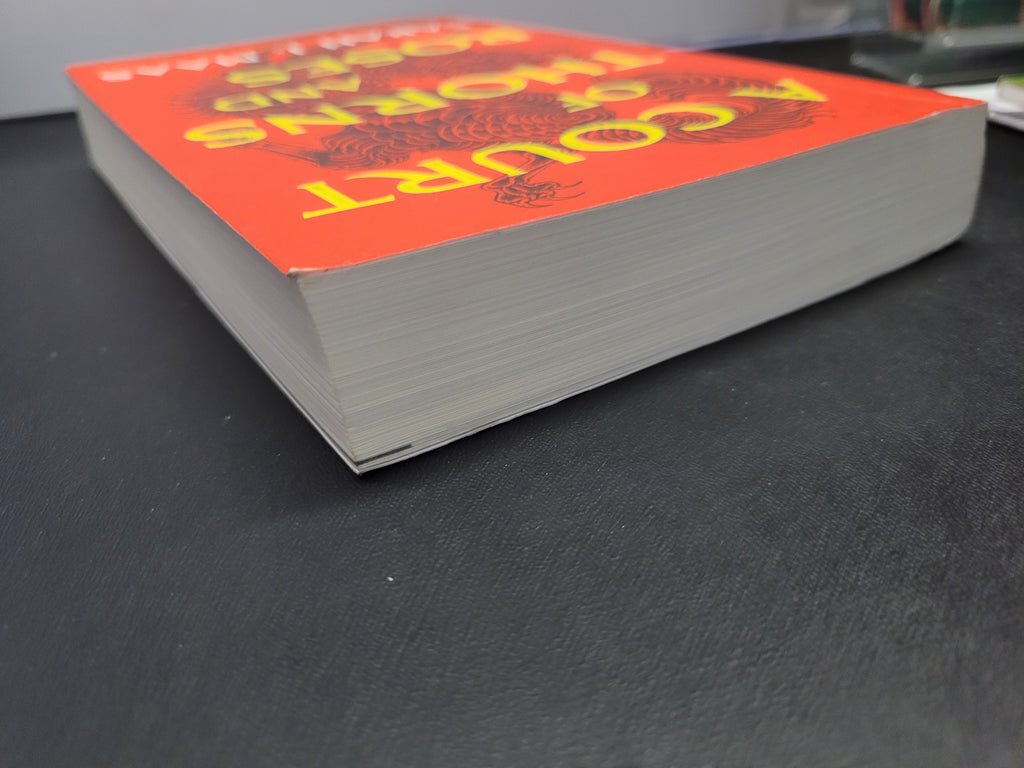 A paperback book "A Court of Thorns and Roses" with a bright orange-red cover and bold yellow title text, photographed at an angle on a dark textured surface.