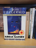 A copy of F. Scott Fitzgerald's 'The Great Gatsby' book standing on a wooden shelf next to other books.