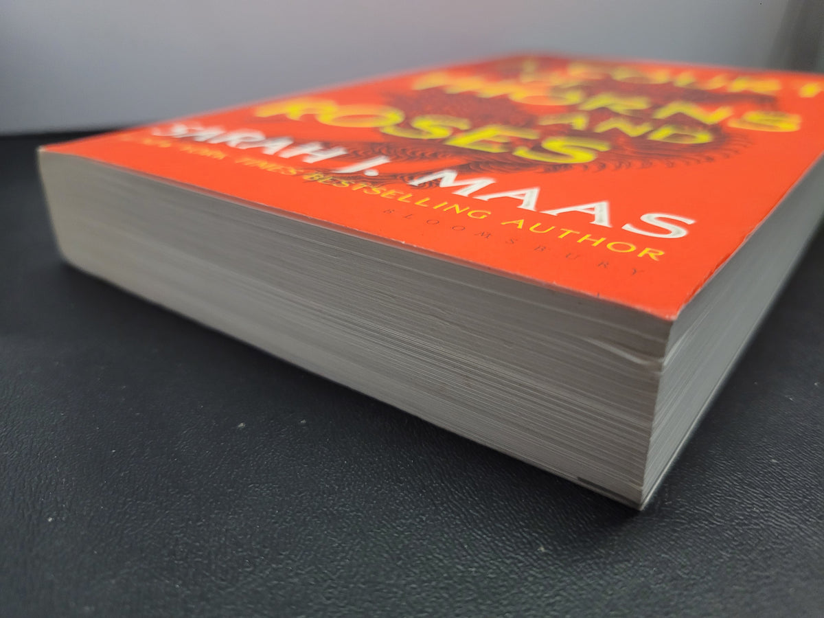 A close-up angled shot of a hardcover book titled 'A Court of Thorns and Roses' by Sarah J. Maas, showing the bright orange cover with yellow and white lettering and the thick white page edges.