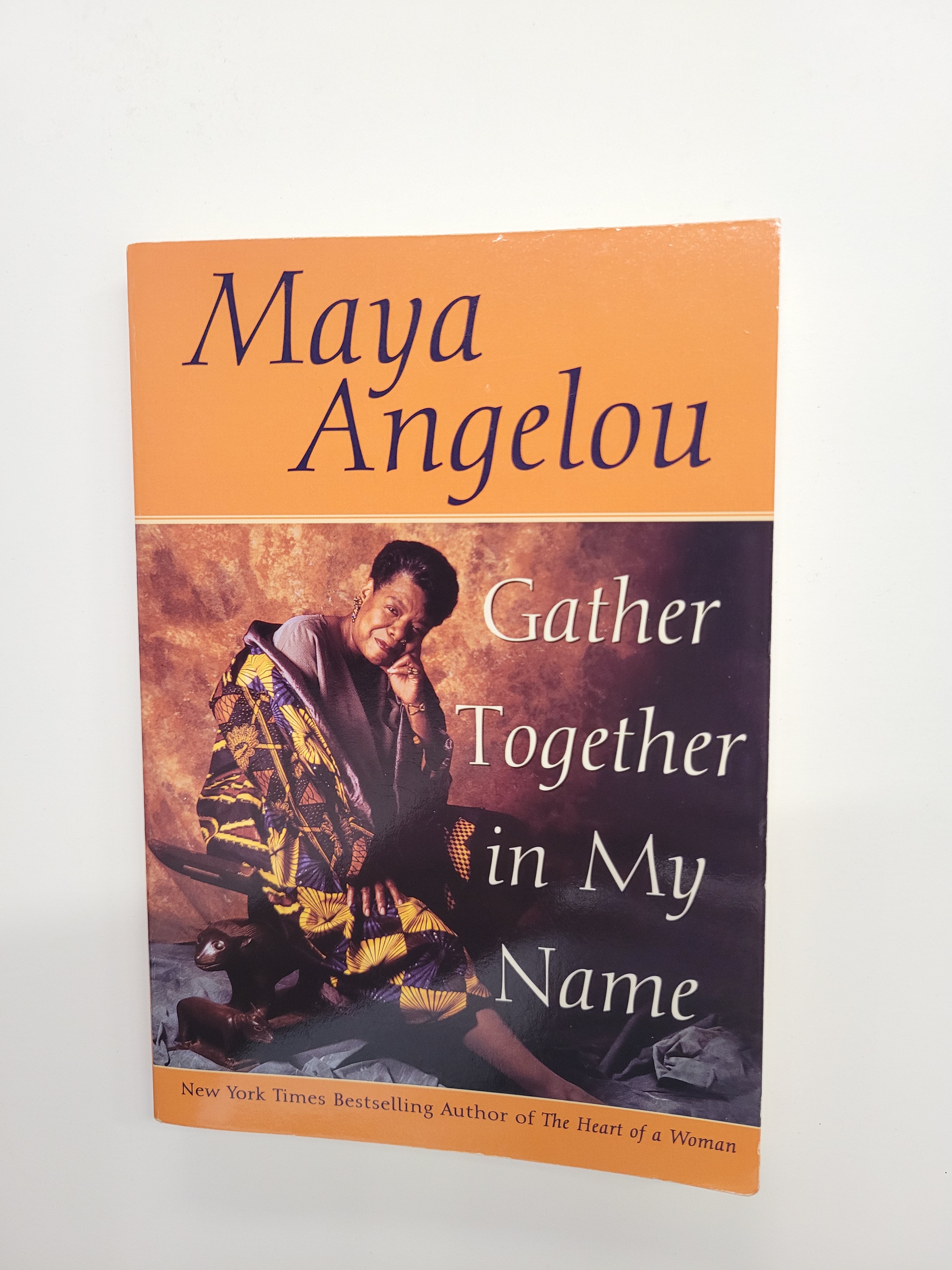 Maya Angelou's book 'Gather Together in My Name' with an orange and dark purple cover, photographed flat against a white background.