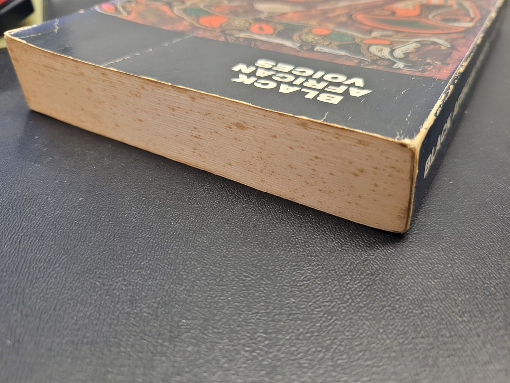 A close-up of a vintage book titled "Black African Voices" showing its worn, tan paper edges and dark cover with an illustrated design, resting on a dark textured surface.