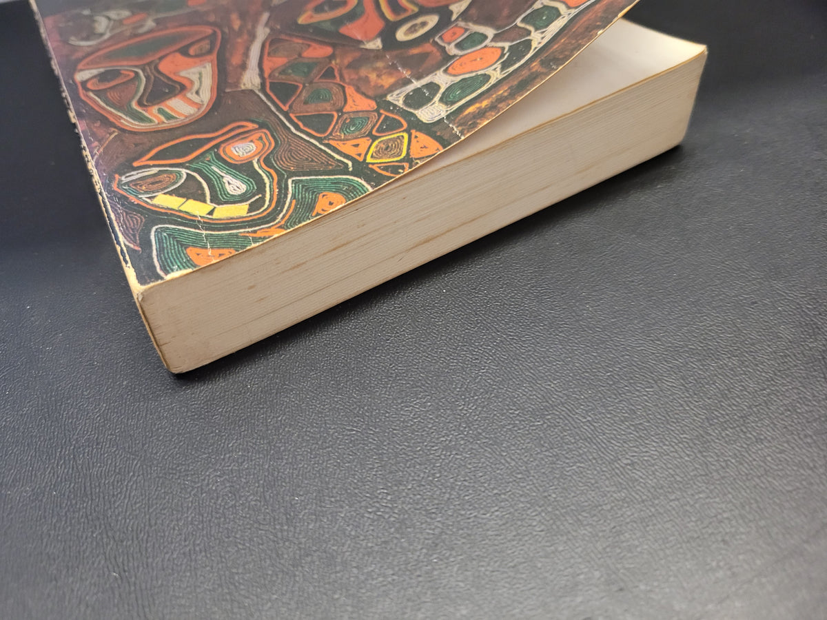 A close-up of an antique book "Black African Voices" with a highly detailed, colorful illustrated cover featuring stylized faces and geometric patterns, resting on a dark textured surface.