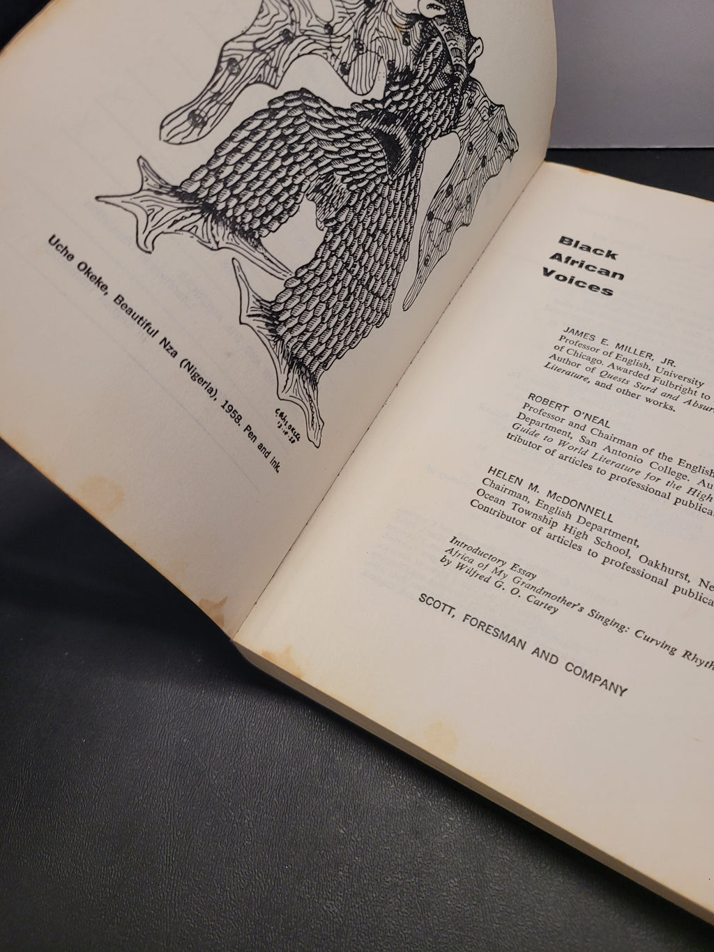 An open vintage book showing printed pages with a black line drawing of a figure and the title 'Black African Voices,' photographed on a dark surface.