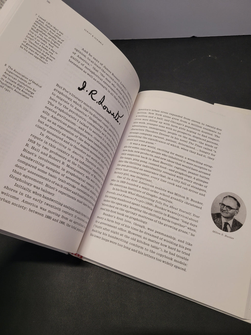 An open book showing printed text pages with a small circular portrait photo and a handwritten signature on one page, photographed on a dark surface.