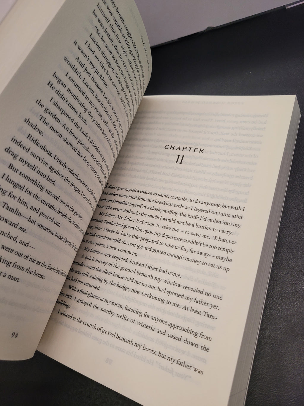 An open book "A Court of Thorns and Roses" showing printed text on both pages, photographed from above on a dark surface. The right page has the heading 'CHAPTER 11' at the top.