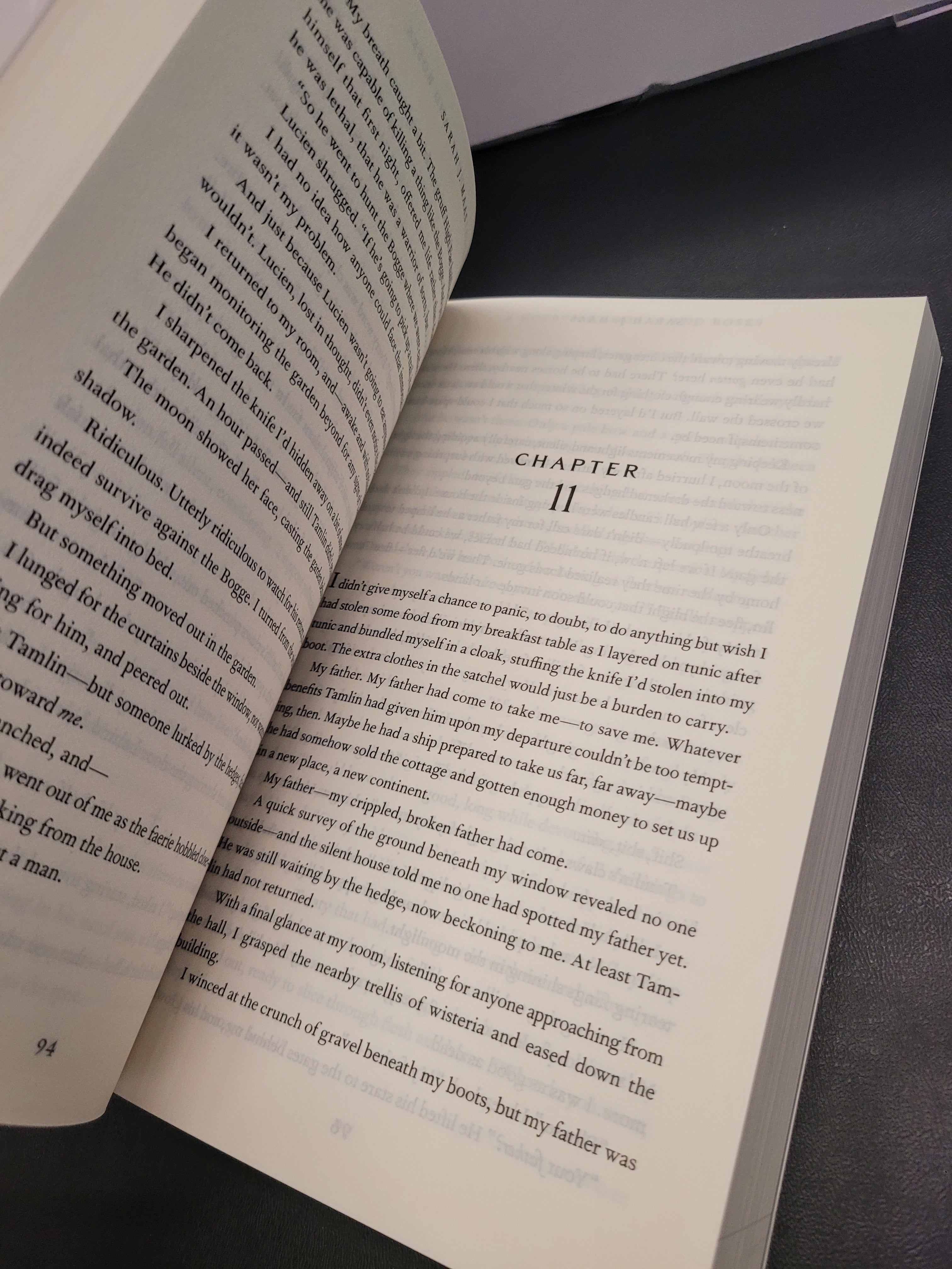 An open book "A Court of Thorns and Roses" showing printed text on both pages, photographed from above on a dark surface. The right page has the heading 'CHAPTER 11' at the top.