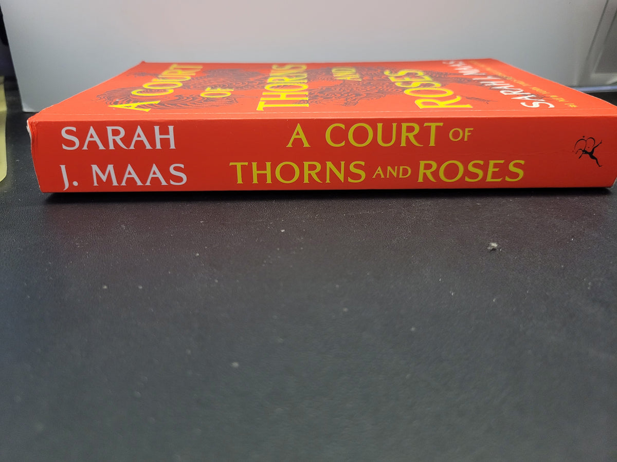 A book titled 'A Court of Thorns and Roses' by Sarah J. Maas, showing the orange-red spine with yellow and white text, resting on a dark gray surface.